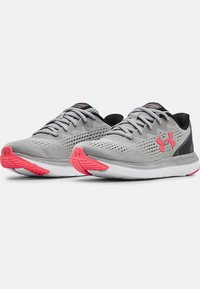 Chaussures de sport grises avec une tige en maille texturée, des accents noirs et une semelle extérieure rose. Dotées de lacets et d'un logo sur le côté. Conçues pour la course.