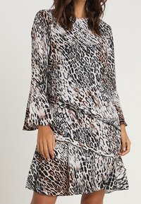 Leopardi-kuosiset mekko pitkillä kellottavilla hihoilla ja kerroksittain rikkoutuvalla helman osalla. Materiaali näyttää kevyeltä ja valuvalta, ja siinä on ruskean ja mustan sekoitus.