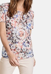 Blusa de manga corta con un patrón geométrico multicolor en rojo, azul y negro, con una textura suave y un cuello redondo.