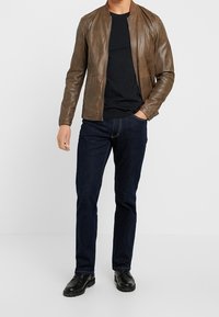 Giubbotto bomber in pelle marrone, t-shirt nera, jeans blu scuro e scarpe nere. Texture liscia, design aderente e stile minimalista.
