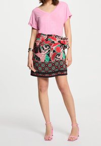 Roze v-hals t-shirt gecombineerd met een bloemenpatroon wikkelrok met rode, groene en zwarte accenten. Model draagt roze sandalen met bandjes.