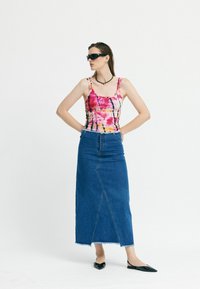 Színes batikolt pántos top, vékony pántokkal, magas derekú farmer maxi szoknyával párosítva. Fekete hegyes orrú balettcipők egészítik ki az öltözéket.