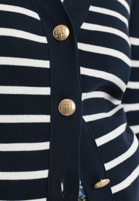 Marineblau- und weiß gestreifter Cardigan aus weichem Strickstoff, mit goldenen Knöpfen und Knopfloch, im klassischen V-Ausschnitt-Design.