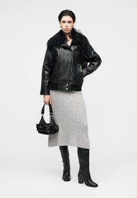 Μαύρο δερμάτινο μπουφάν με γούνινο γιακά, γκρι πλεκτή φούστα, μαύρες μπότες μέχρι το γόνατο και μικρή μαύρη τσάντα με τρουκς και λουριά.