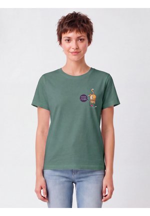 Jonge vrouw met kort haar die een groen T-shirt draagt met een kattenafbeelding en een tekstballon met de tekst "Houston, we have a problem."