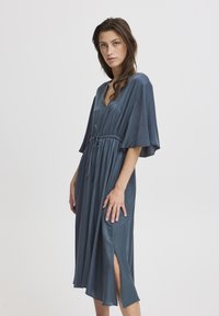 Midikleid aus dunkelblauem Seidenstoff mit kurzen Ärmeln, V-Ausschnitt, verstellbarem Taillenzug und seitlichen Schlitzen für mehr Bewegungsfreiheit.