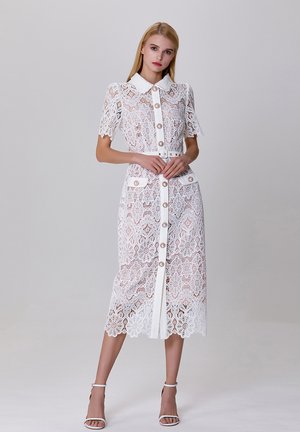 Robe en dentelle blanche avec des manches courtes, un col, une fermeture à boutons à l'avant et des motifs floraux. Dispose d'une taille ceinturée et de deux poches.