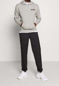 Sweat à capuche gris avec une poche avant et des cordons blancs, arborant un logo coloré. Associé à un pantalon noir et des baskets blanches.