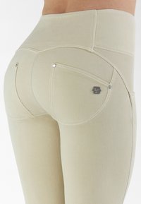 Leggings beige a vita alta in tessuto strutturato, con doppie tasche posteriori e dettagli in metallo argentato.