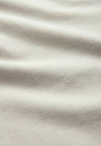 Baumwolllenstoff mit einer weichen, glatten Textur in einem hellen Beigeton, der subtile Falten und ein feines Gewebe-Muster aufweist.