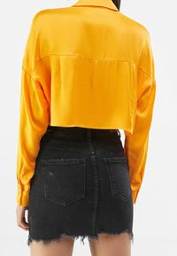 Avskuren gul sating shirt med långa ärmar, parat med en svart denimkjol med fransad nederkant och två bakfickor.