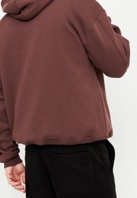 Felpa con cappuccio marrone dal finish testurizzato, con orlo e polsini a coste, abbinata a pantaloni neri con tasche posteriori.