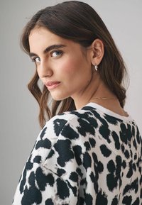 Maglione con stampa leopardata e scollatura a girocollo, caratterizzato da nero su uno sfondo beige. Il modello mette in mostra gioielli delicati e capelli texturizzati.