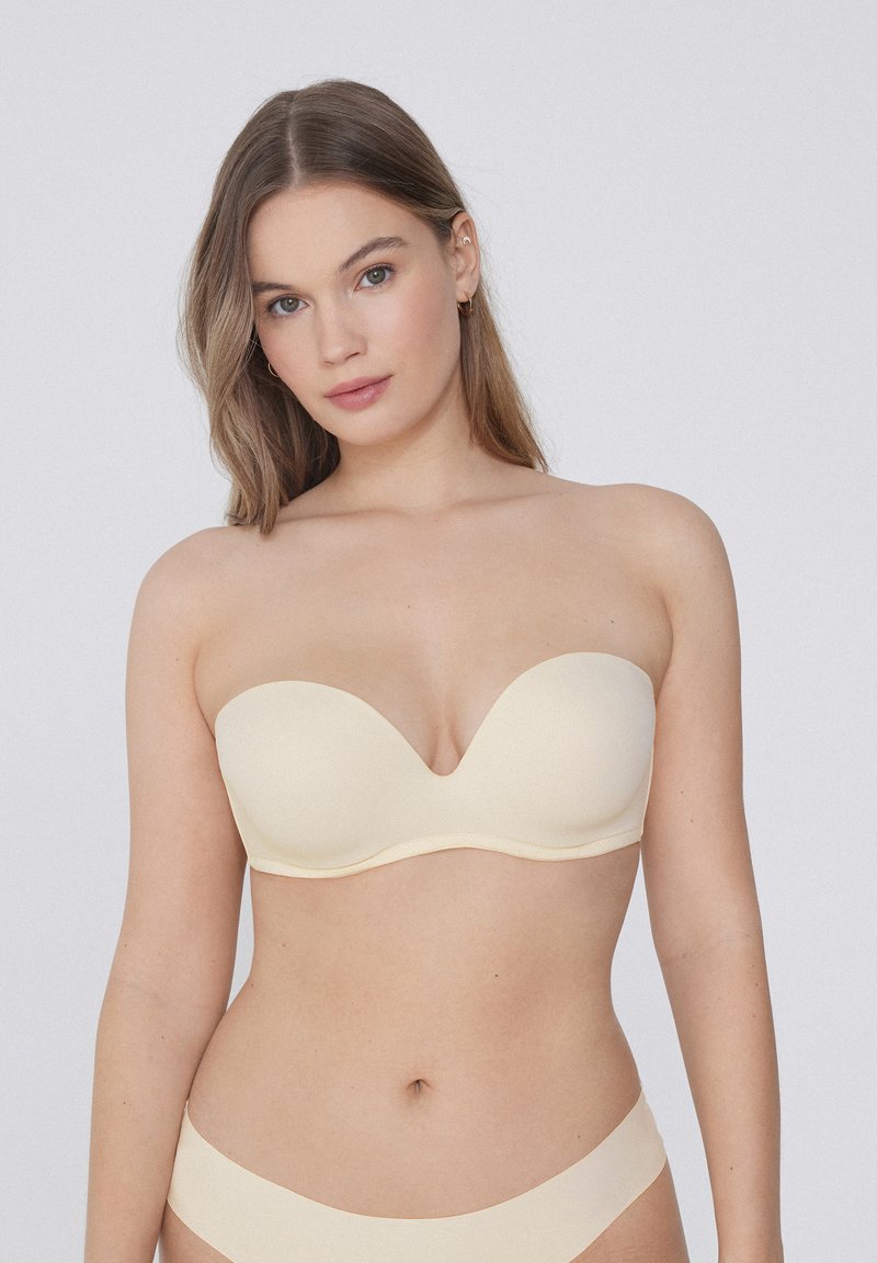 Draagbare beige bh zonder bandjes met een gladde, naadloze ontwerp en lichte padding, met een subtiele glans en zonder zichtbare hardware of accenten.