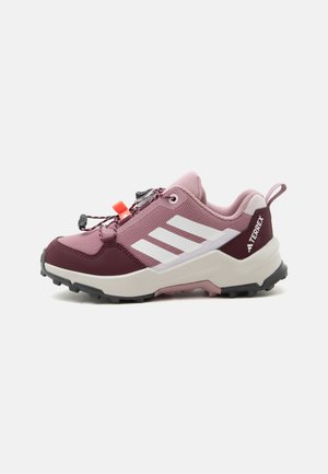 Chaussure de trail running rose et bordeaux avec des rayures blanches, semelle noire robuste, languette de traction et système de laçage rapide sur fond neutre.