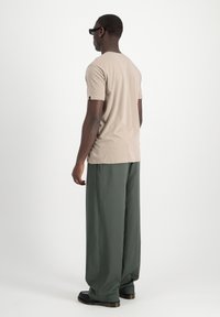 Camiseta de manga corta beige con cuello redondo, combinada con pantalones holgados de color verde oscuro. El conjunto tiene un ajuste relajado y un diseño sencillo.