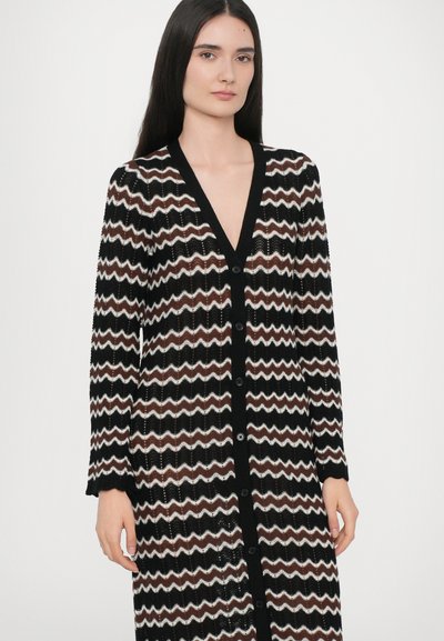 Zwart en crèmekleurige zigzagpatroon cardigan met een diepe V-hals, lange mouwen en knoopsluiting, met een losse, gebreide textuur.