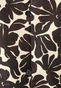 Tissu imprimé floral noir avec de grands pétales abstraits et deux boutons noirs sur fond beige.