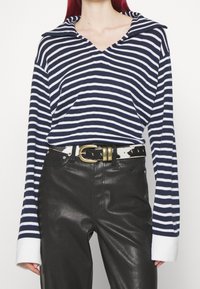 Marineblauw en witte gestreepte gebreide top met een V-hals en een oversized kraag, gecombineerd met zwarte nepleren broek en een patroongordel met een gouden gesp.
