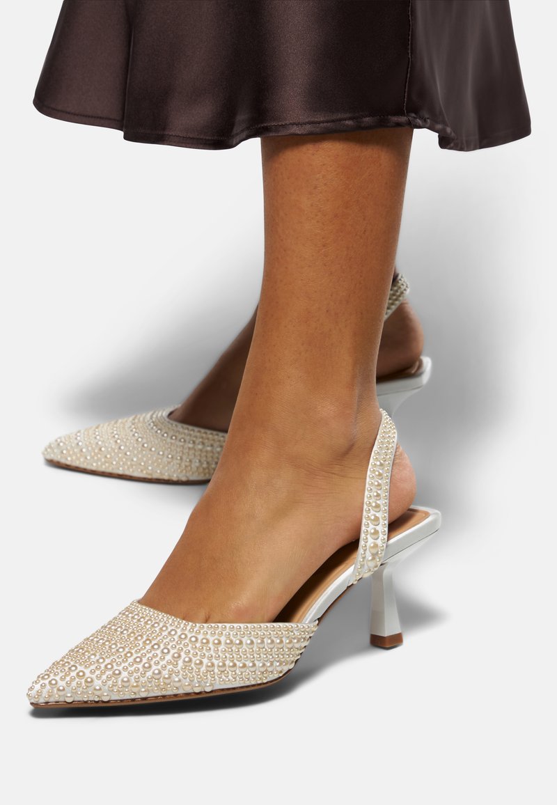 Bílé slingback podpatky s špičatou špičkou, ozdobené malými kulatými perlami, s blokovým podpatkem střední výšky a hladkým povrchem.