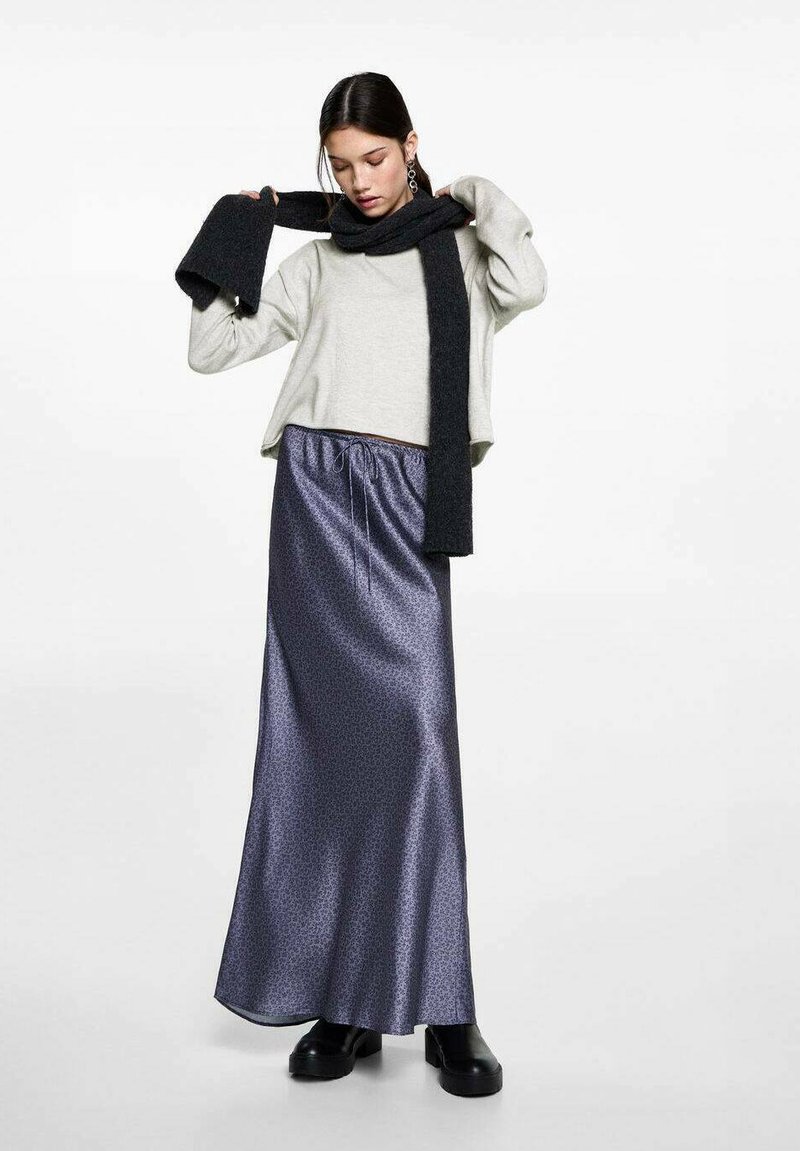 Vaalea harmaa lyhytnenäinen neule, musta neulottu huivi ja pitkä, kiiltävä tumma sininen hame, jossa on nauhavyötärö. Mustat tukkikengät viimeistelevät asun.