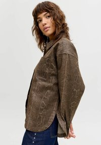 Brūna krekla žakete ar čūskas rakstu, ar vaļēju piegriezumu, apkakli, vienu krūšu kabatu un sānu šķēlumiem ērtai kustībai.