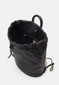 Černá kožená taška na stažení s hladkým povrchem, zlatými detaily a vnitřní kapsou na zip. Disponuje zaoblenou rukojetí a řetízkovým popruhem.