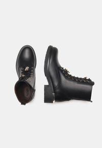 Bottines en cuir noir avec bouts ronds, lacées sur le devant, accents en métal doré, semelles texturées et petit talon bloc.
