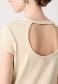 Beige ribbed top featuring short sleeves and a round open back design. Smooth texture with finished edges, highlighting the back detail.