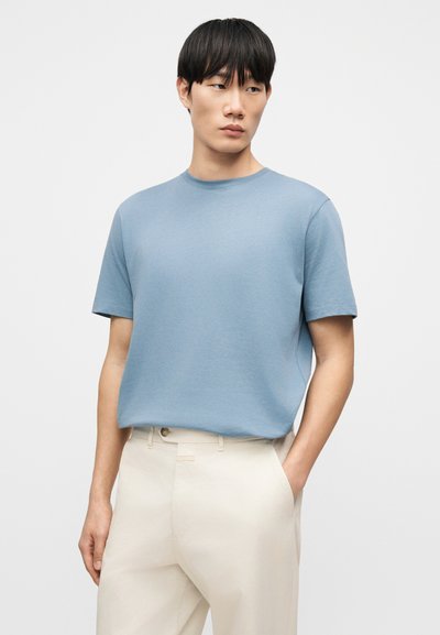 Ανοιχτό μπλε κοντομάνικο μπλουζάκι κατασκευασμένο από λεία υφάσματα, με στρογγυλή λαιμόκοψη. Συνδυασμένο με παντελόνια σε κρεμ χρώμα.