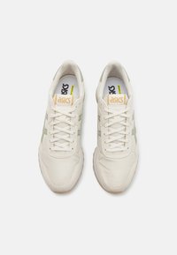 Baltie sporta apavi ar zaļiem akcentiem, teksturēta sintētiskā virsma, auklu aizdare, mīkstināta apkārtne un gumijas zole. ASICS zīmols uz mēles.
