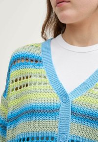Stickad kappa med horisontella ränder i ljusblått, grönt och grått. Öppen vävstruktur med V-ringning och blå knappar.