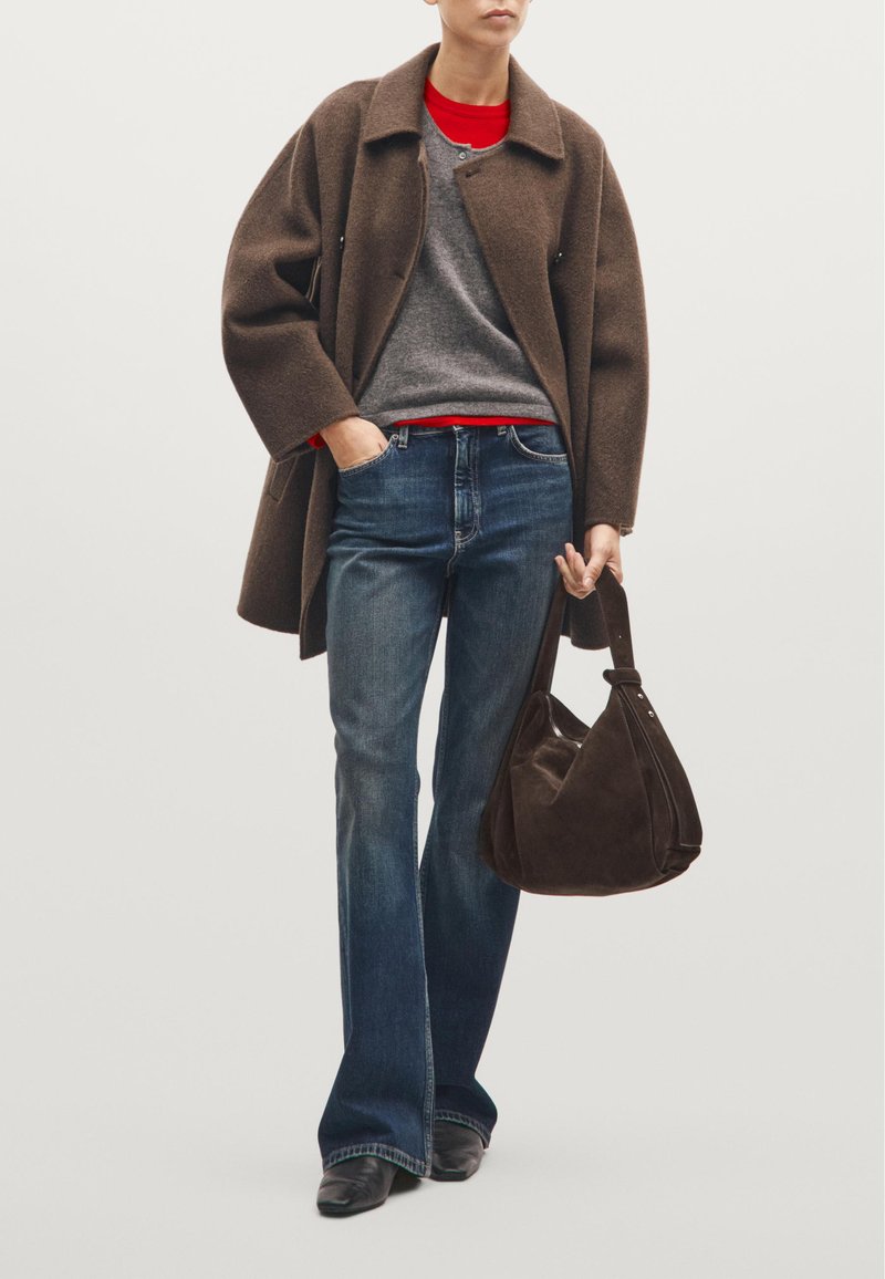 Brązowy wełniany płaszcz, szary sweter, czerwona koszula, dżinsowe spodnie i brązowa zamszowa torebka. Dzwony i czarne botki za kostkę dopełniają wygląd.