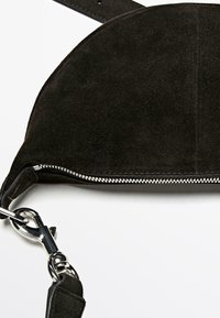 Schwarze Wildledertasche mit gewölbtem oberen Teil, silbernem Reißverschluss und silberner Schnalle. Verfügt über einen abnehmbaren Riemen für vielseitige Tragemöglichkeiten.