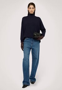 Marinblå polotröja, ljusblå utsvängda jeans, mörkbruna handskar och en svart clutchväska. Mjuka texturer med en avslappnad passform.