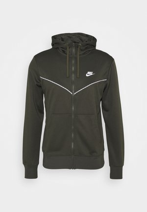 Donkergroene Nike hoodie met ritssluiting, capuchon, trekkoorden, voorzakken en witte reflecterende chevronstrepen over de borst en schouders.