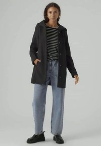 Black waterproof jacket with a hood, snap buttons, four pockets; worn over a striped shirt and light blue wide-leg jeans. Black shoes.
