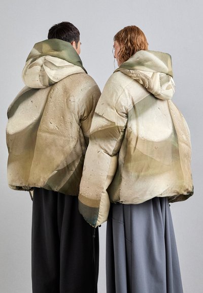 Puffer jackets in beige with green and brown abstract patterns, featuring hoods and elastic hems, worn over dark and light-colored clothing.