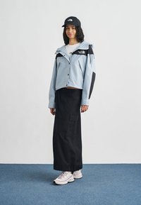 Ανοιχτό γαλάζιο cropped σακάκι με μαύρες λεπτομέρειες, μακριά μαύρη φούστα και λευκά αθλητικά παπούτσια. Το σύνολο έχει έναν casual σχεδιασμό κατάλληλο για εξωτερική χρήση.