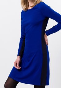 Abito a maniche lunghe con un vivace corpo blu e pannelli laterali neri, realizzato in tessuto morbido, con scollatura rotonda e vestibilità ampia.
