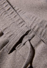 Grijze stof met een gestructureerd oppervlak, met geplooide plooien en zichtbare stiksels. Het ontwerp heeft een platte tailleband met een lusdetail.