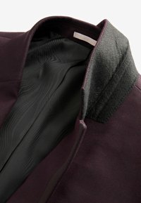Burgundowa podszewka kurtki z gładką czarną podszewką, z szarym filcowym kołnierzem i subtelnymi teksturowanymi detalami na materiale.