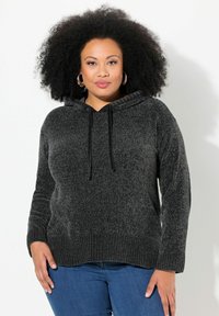 Zwarte, gestructureerde hoodie met een trekkoord in de capuchon, geribde manchetten en zoom, gedragen over blauwe spijkerbroeken.