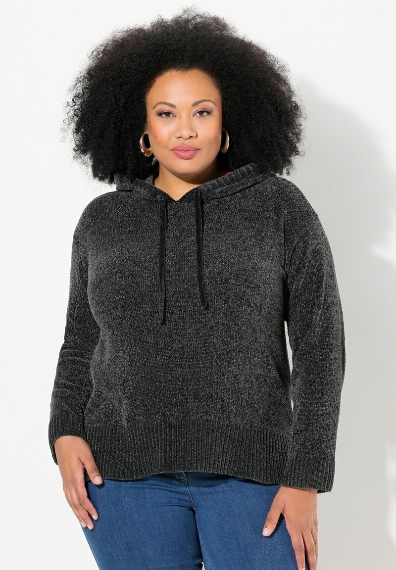 Zwarte, gestructureerde hoodie met een trekkoord in de capuchon, geribde manchetten en zoom, gedragen over blauwe spijkerbroeken.