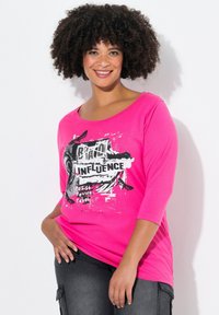 Rosa Baumwoll-T-Shirt mit Rundhalsausschnitt, dreiviertellangen Ärmeln und einem grafischen Druck mit schwarzem Text und Spritzdesign.
