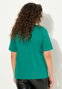 T-shirt verde a maniche corte in tessuto morbido, con vestibilità rilassata e scollatura tonda semplice. Retro semplice con texture liscia e senza ornamenti.