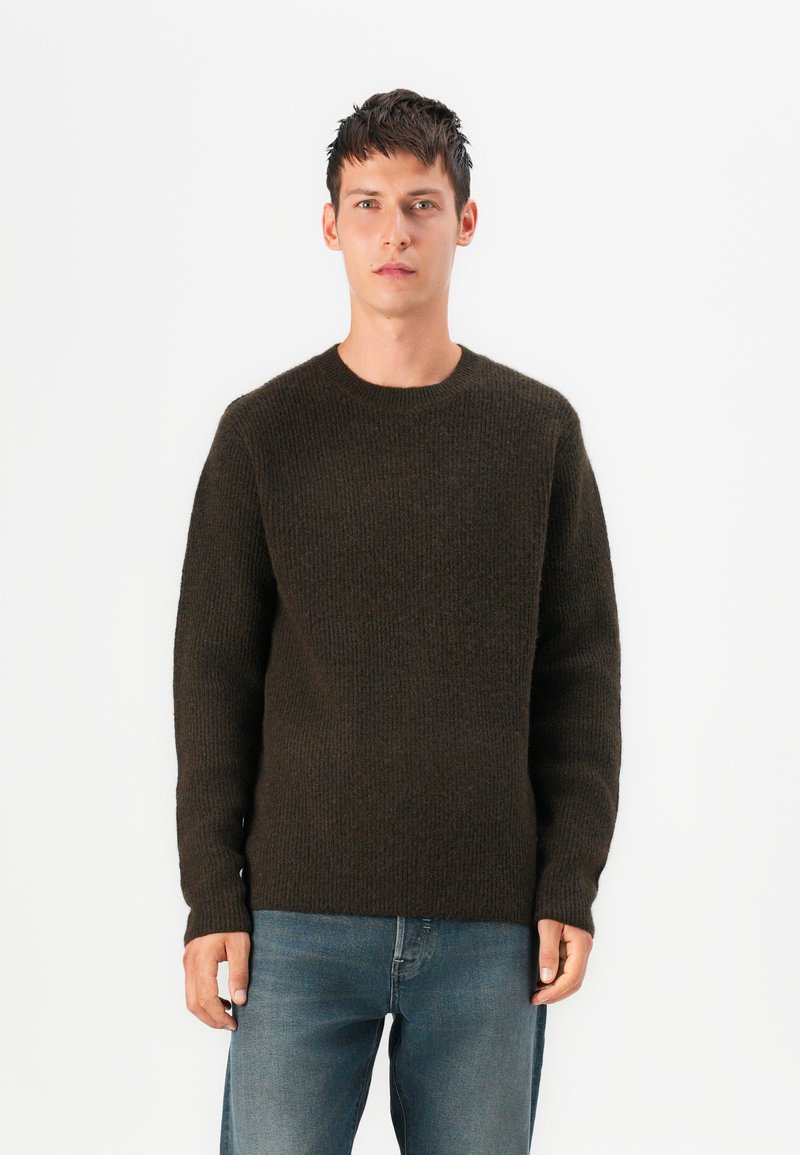 Pulôver de malha castanho escuro com gola redonda e mangas longas, apresentando um padrão texturizado e punhos em canalé. Combinado com jeans azuis.