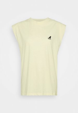 Beżowy, bezrękawnikowy t-shirt bez rękawów z wyściełanymi ramionami i małym czarnym logo kangura na lewej piersi.