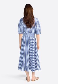 Abito midi a righe blu e bianche con vita cinchata, maniche corte e gonna svasata. Sandali piatti completano il look.