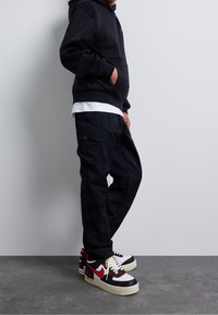 Černá mikina s kapucí a přední kapsou, kombinovaná s tmavými cargo kalhotami a červenými, černými a bílými teniskami Nike Air Force 1.